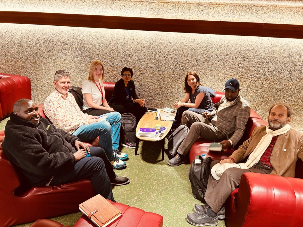A group of seven people sitting in a cozy lounge on red sofas, engaged in conversation around a small table.