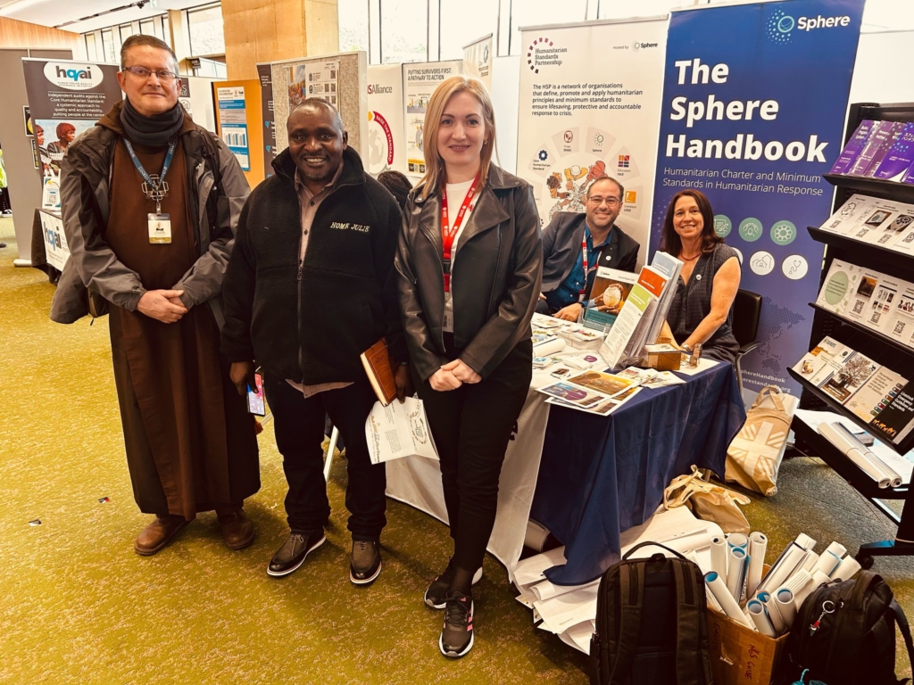Three individuals stand infront of a table while two others sit at the Sphere booth during the HNPW.